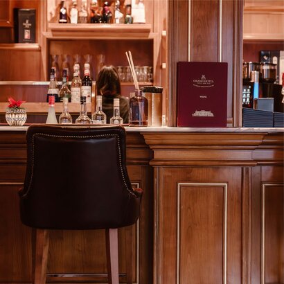 Eine leere Hotelbar mit Holztresen, Flaschen und einem Menü im GRAND HOTEL Zell am See.