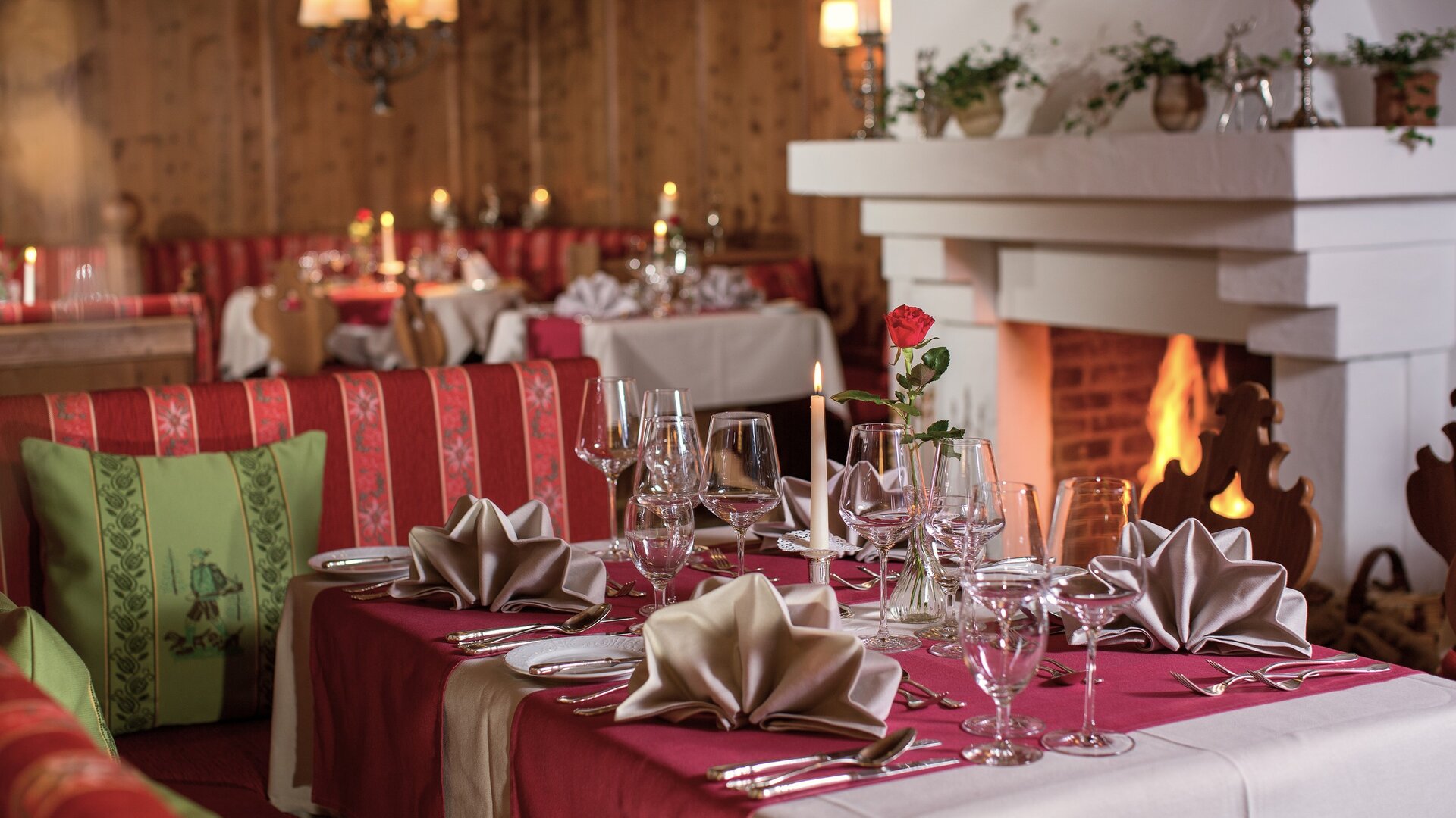 Ein elegant gedeckter Tisch mit roter Tischwäsche steht vor einem Kamin im Hotelrestaurant.