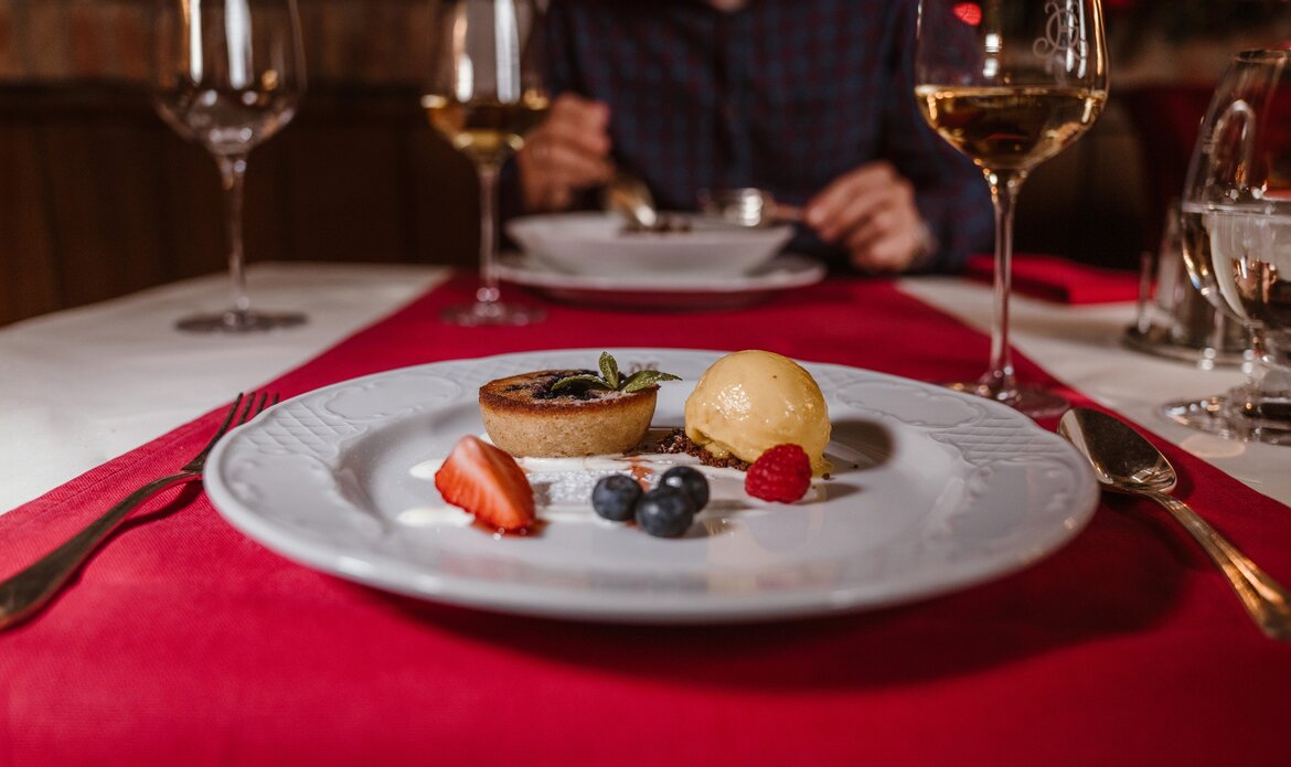 Ein Dessertteller mit Gebäck, Eis und Beeren liegt auf einem rot gedeckten Tisch im Hotelrestaurant.