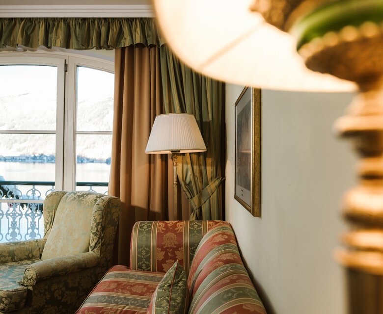 Ein gemütlicher Wohnbereich mit Sofa und Sessel, daneben Balkontüren mit Blick auf den See.