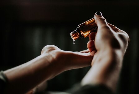 Wellnessöl auf den Händen im GRANDSPA Eine Hand hält ein Fläschchen mit Öl über einer offenen Handfläche, aus der ein Tropfen auf die Haut fällt.