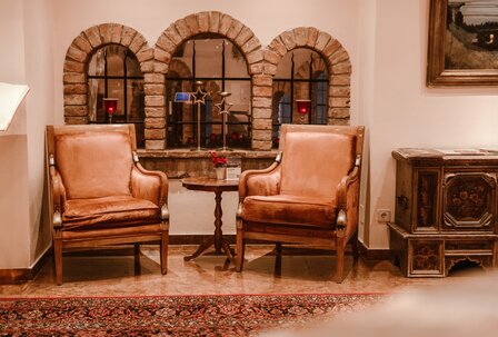 Hotel-Lounge mit Ledersesseln und Kaminfenster Zwei Ledersessel stehen vor einer gemauerten Kaminnische mit drei Bogenfenstern und einem kleinen Tisch dazwischen.