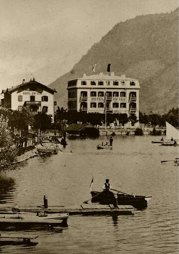 Ein historisches Hotelgebäude steht direkt am Ufer des Zeller Sees, davor liegen mehrere Ruderboote im Wasser.