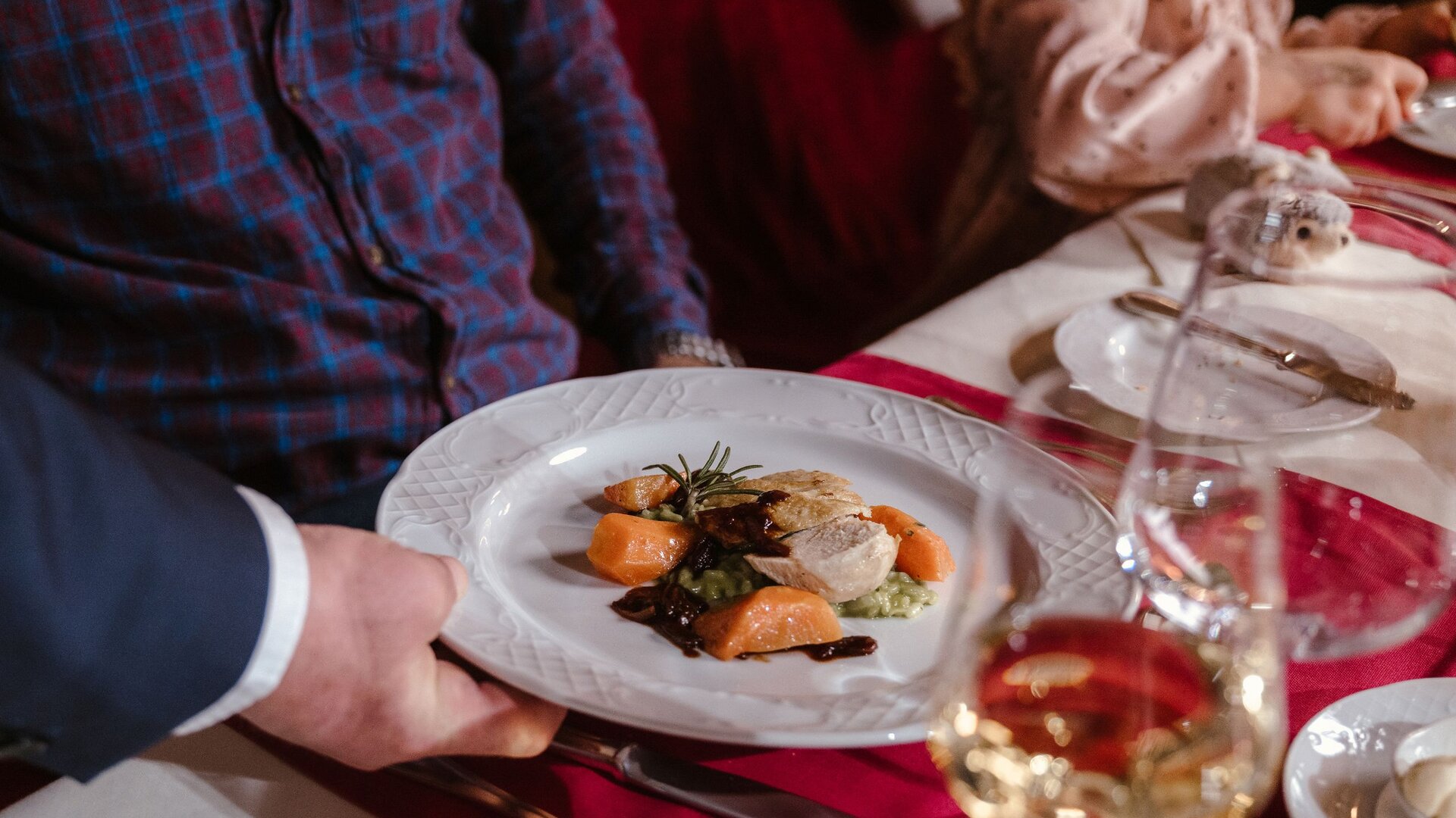 Ein Kellner reicht einen Teller mit angerichtetem Abendessen am gedeckten Tisch im Hotelrestaurant.