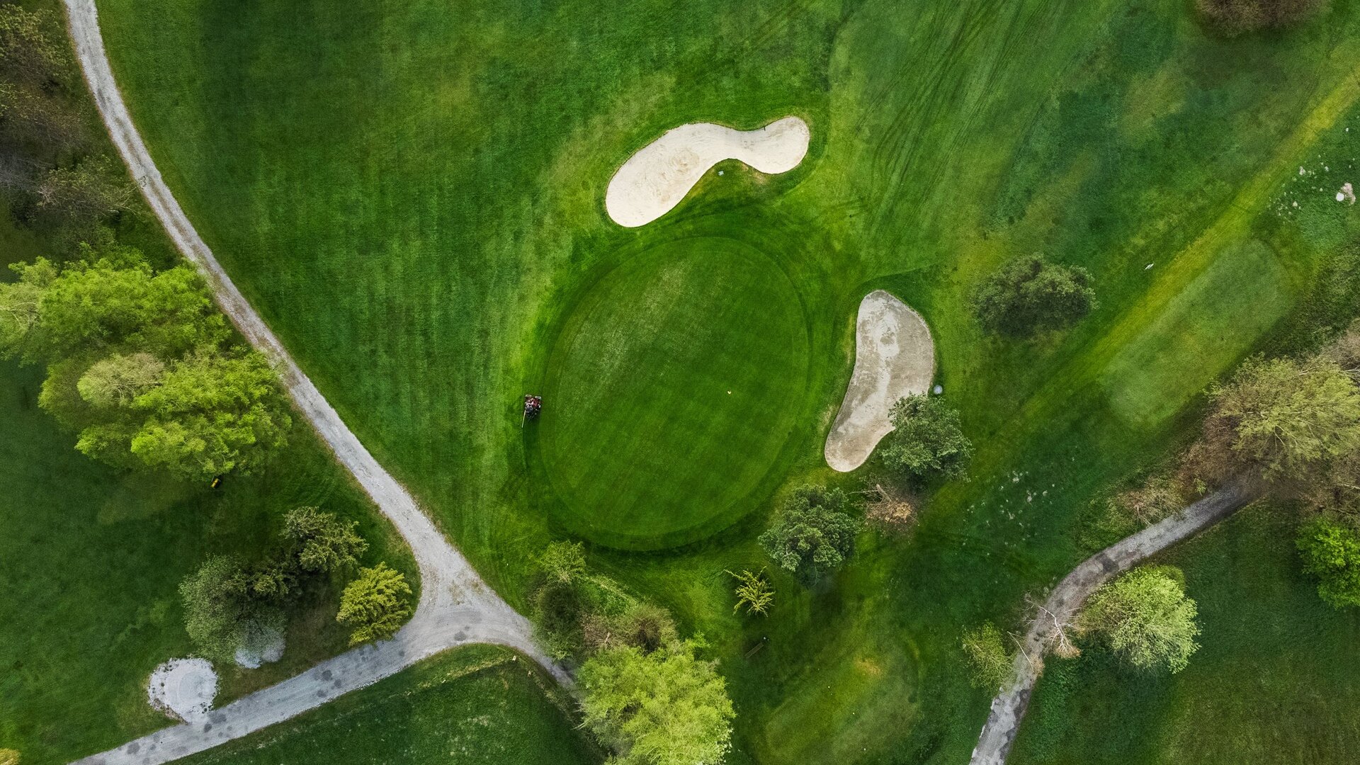 Eine Luftaufnahme zeigt ein Golfloch mit Abschlag, Fairway und zwei Bunkern in grüner Landschaft.
