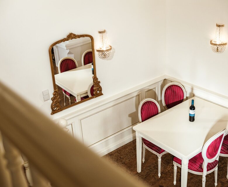 Ein kleiner Sitzbereich mit weißem Tisch, rosafarbenen Stühlen und Spiegel in einem hellen Hotelzimmer.