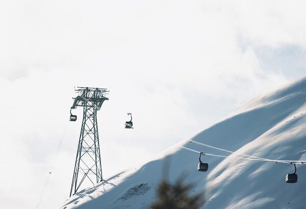 Mehrere Skigondeln schweben über einen verschneiten Hang unter hellem Winterhimmel.