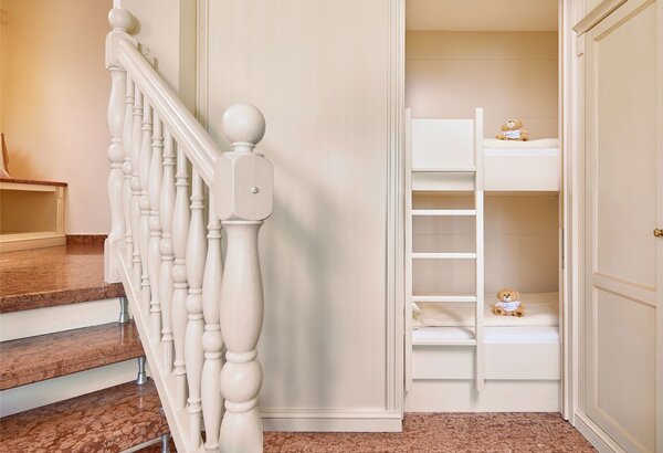 Ein heller Flur mit einer weißen Holztreppe und einem eingebauten Etagenbett mit Kuscheltieren.