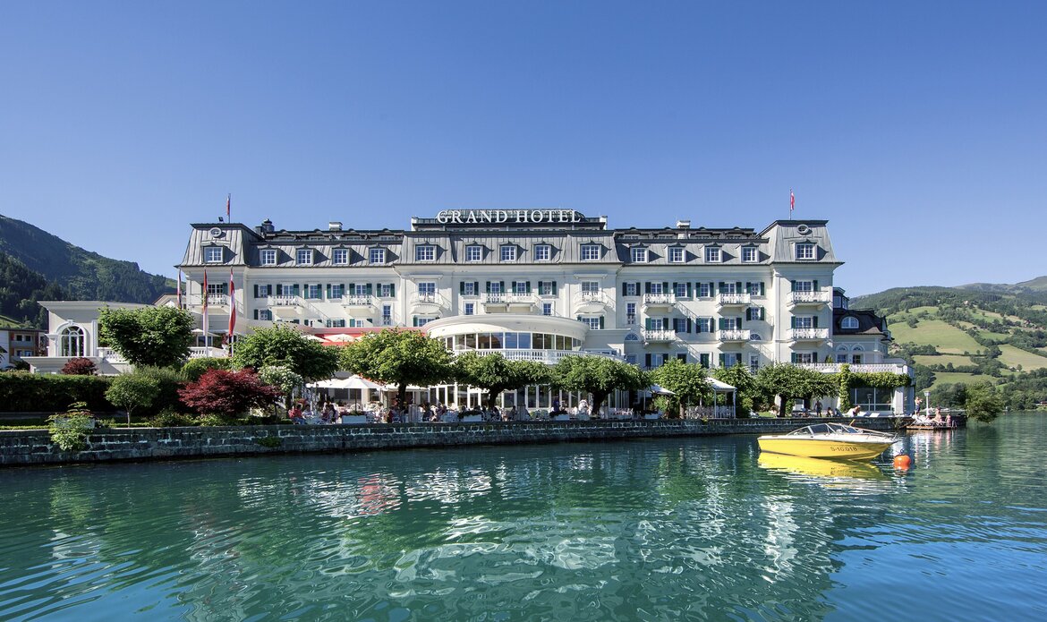Das GRAND HOTEL Zell am See liegt direkt am Wasser mit Terrasse, Steg und Blick auf die Berge im Hintergrund.