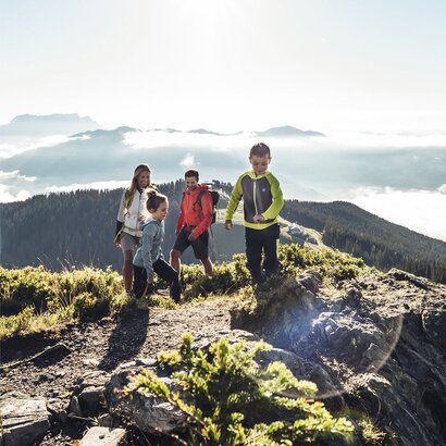 Eine Familie wandert mit zwei Kindern auf einem felsigen Bergpfad mit Blick über die Berge.