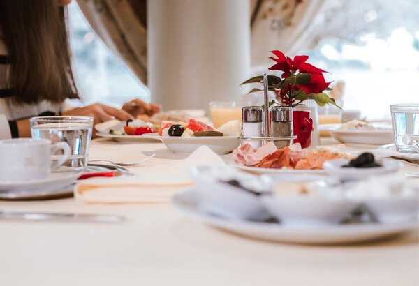 Ein gedeckter Frühstückstisch mit Brot, Aufschnitt, Marmelade und Getränken in einem hellen Hotelrestaurant.