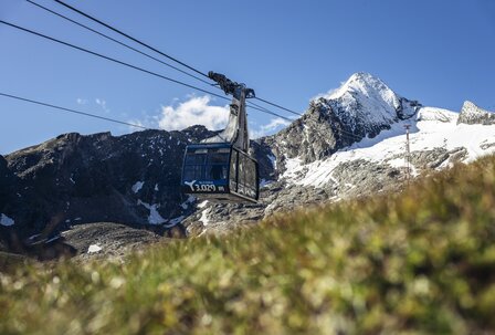 Seilbahn zur Schneelandschaft am Berg Eine Seilbahnkabine fährt vor einer verschneiten Bergkulisse unter einem klaren blauen Himmel.
