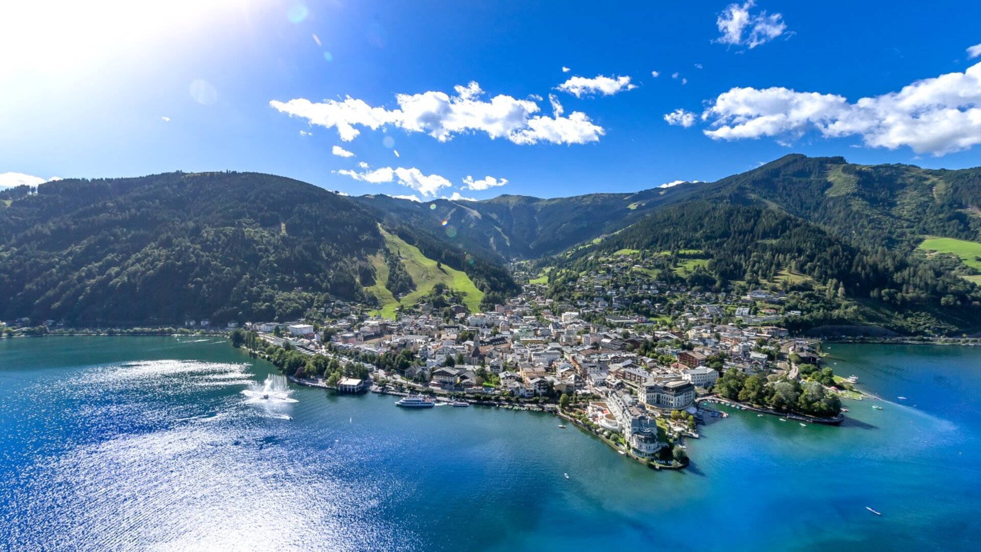 A view across Lake Zell toward Zell am See, with mountains, green slopes and a few boats on the water.