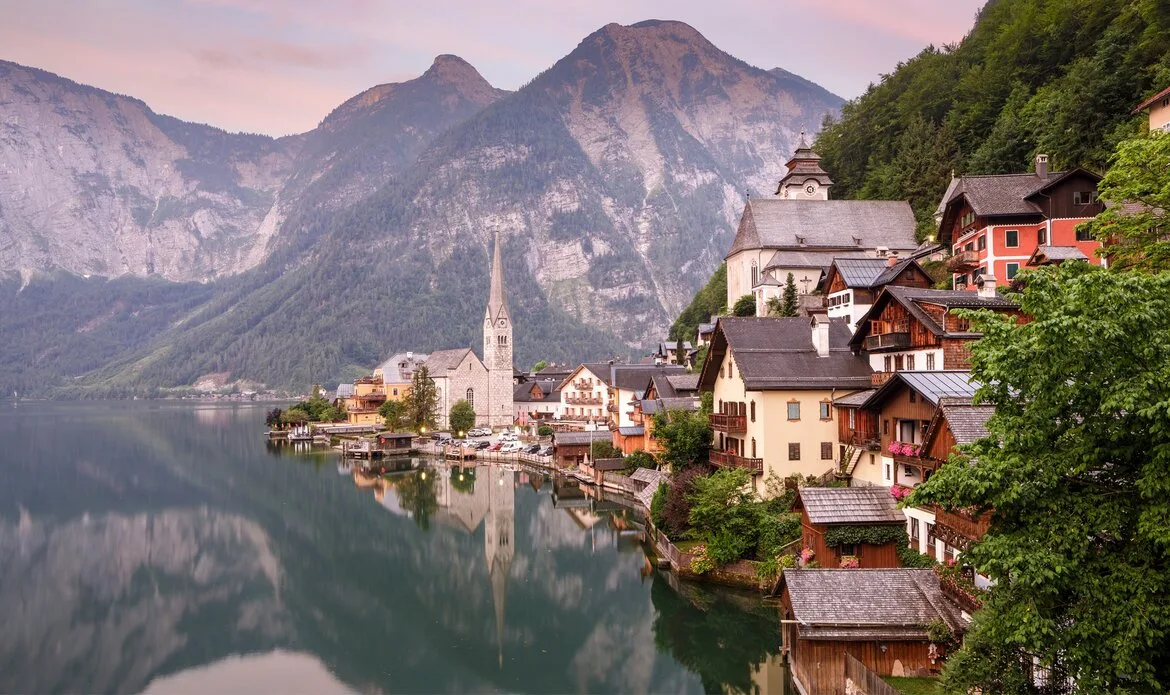 Der Ort liegt am Ufer eines ruhigen Sees vor Bergen und spiegelndem Wasser.