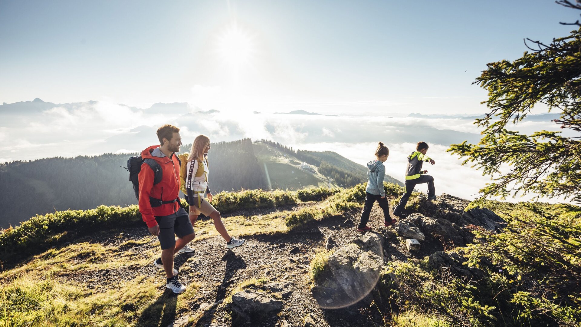 Vier Wanderer stehen auf einem Bergpfad mit Blick über die Alpen und den See im Morgenlicht.