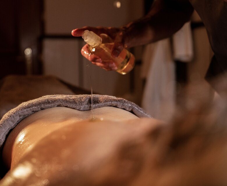 Eine Wellnessbehandlung, bei der Öl auf den Rücken einer liegenden Person aufgetragen wird.