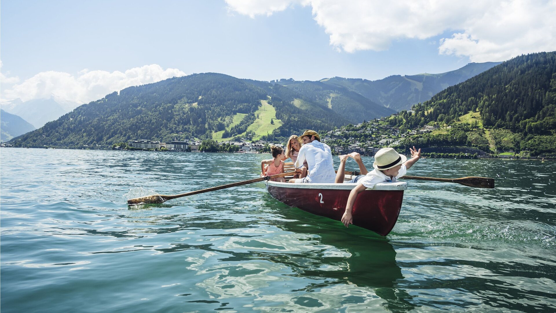 Eine Familie rudert in einem roten Boot auf dem Zeller See vor der Bergkulisse.