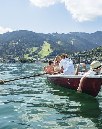Eine Familie rudert in einem roten Boot auf dem Zeller See vor der Bergkulisse.