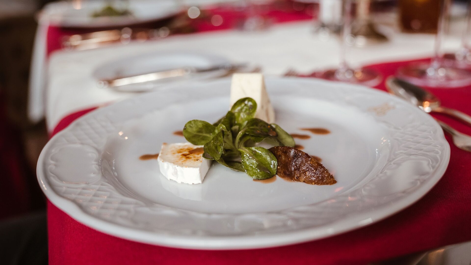 Eine feine Vorspeise mit Ziegenkäse, Basilikum und Sauce auf einem weißen Teller im Hotelrestaurant.