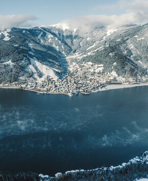 Der Zeller See liegt im Winter vor verschneiten Bergen und dem Ort Zell am See.