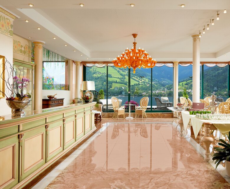 Ein heller Hotel-Loungebereich mit großen Fenstern, poliertem Marmorboden und Blick auf die Berge.