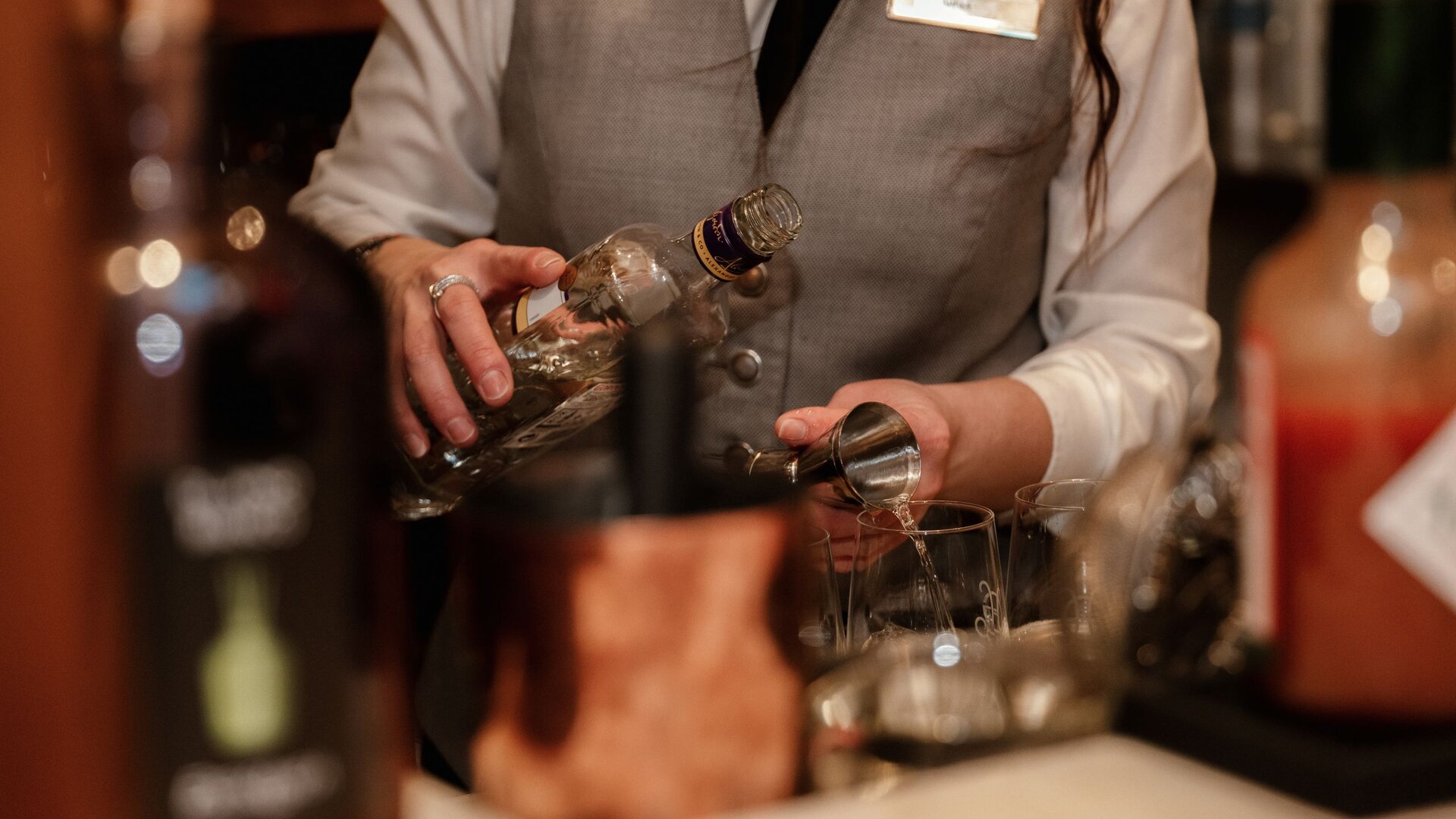 Eine Mitarbeiterin schenkt an der Bar einen Drink aus und füllt ein Glas im GRAND HOTEL Zell am See.