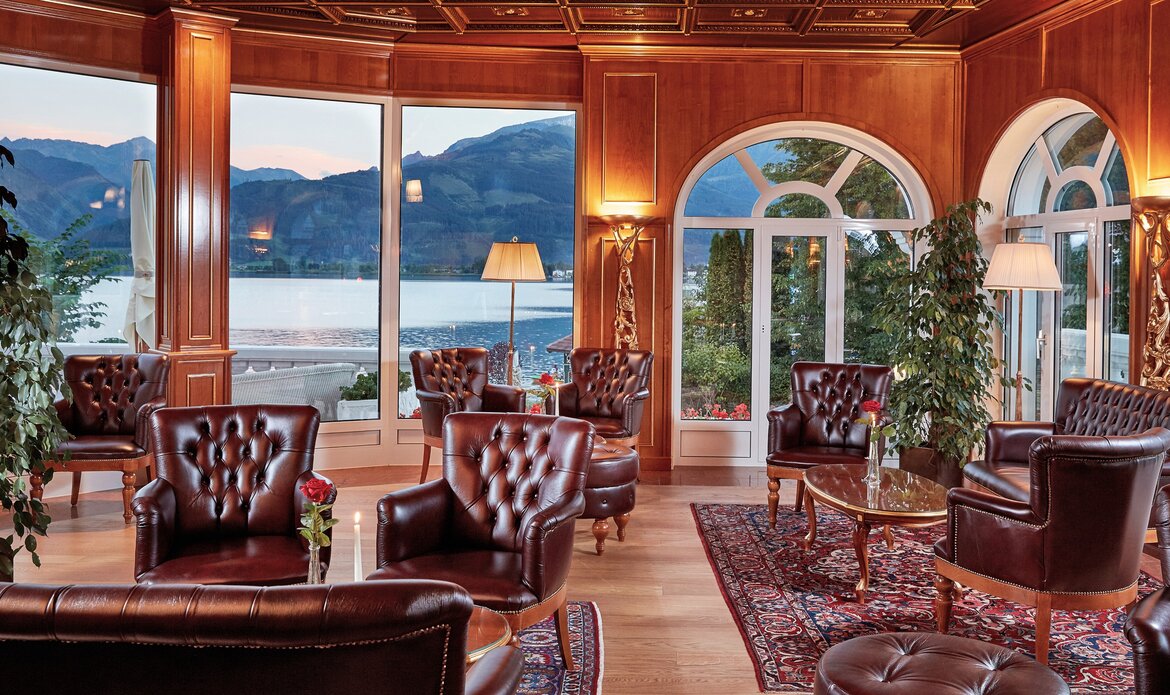 Elegante Sitzgruppe in der Hotelbar mit großen Fenstern zum See und den Bergen im Hintergrund.