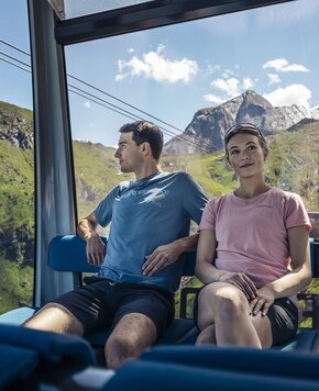 Ein Paar sitzt in der Gondel und blickt auf Berge und Himmel während der Fahrt am Zeller See.