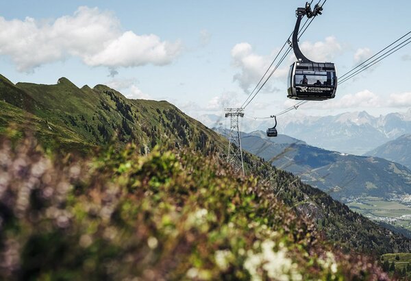 A cable car glides above a green mountain landscape with a wide view into the valley.