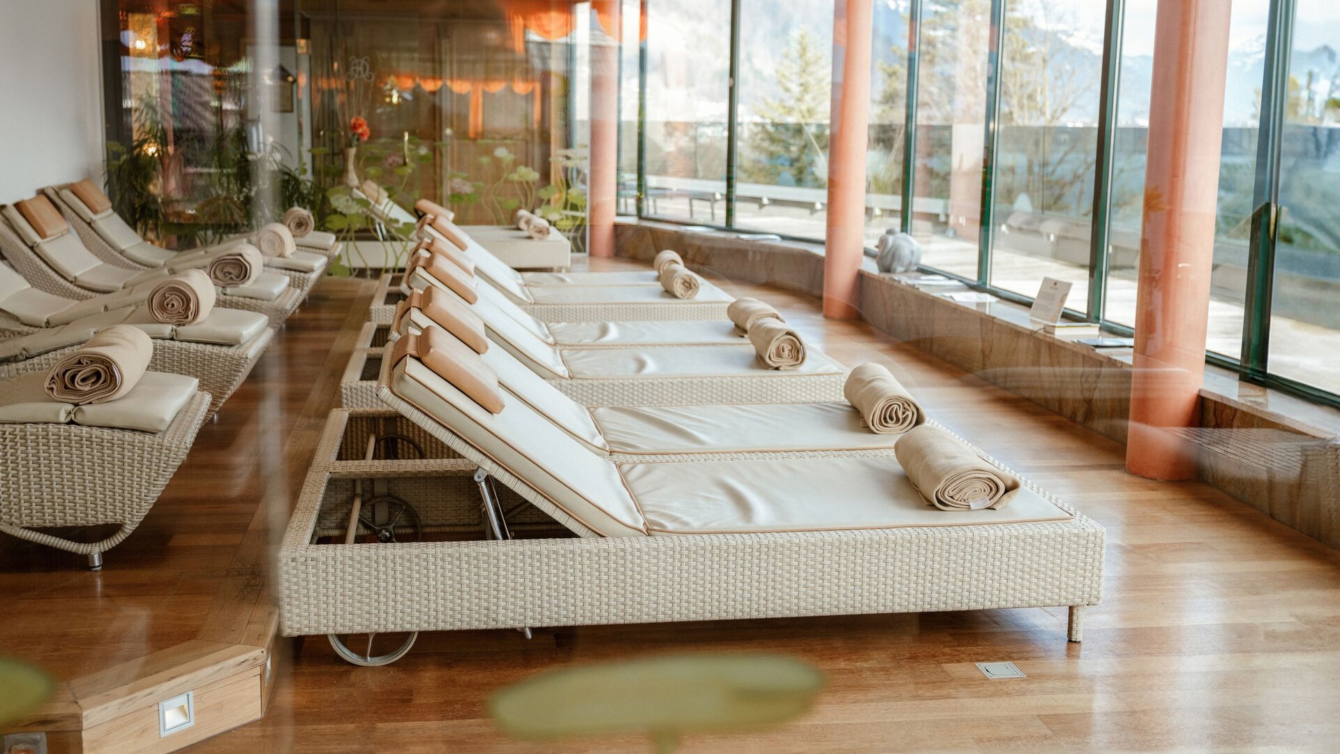 Reihen von Liegen mit Rollliegen in einem hellen Spa-Bereich mit großen Glasfronten.