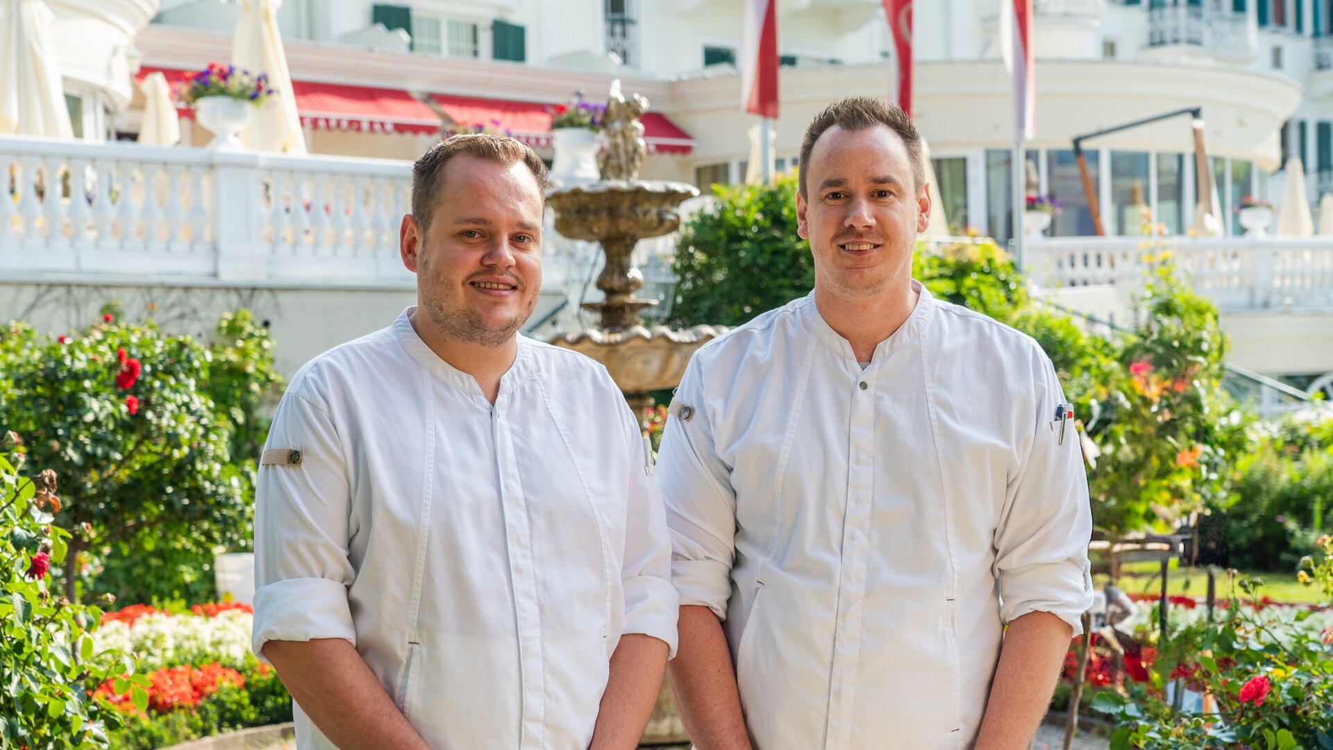 Zwei Hotelmitarbeiter stehen im Garten vor dem GRAND HOTEL Zell am See.