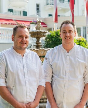 Zwei Hotelmitarbeiter stehen im Garten vor dem GRAND HOTEL Zell am See.