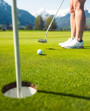 Eine Golferin puttet den Ball auf dem Grün, während Fahne und Loch im Vordergrund zu sehen sind.