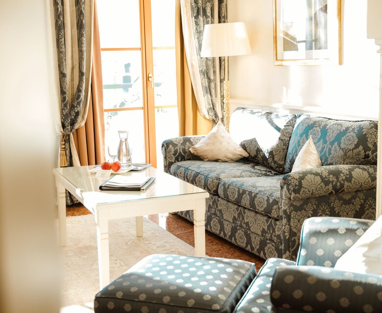 Ein heller Wohnbereich einer Suite mit Sofa, Couchtisch und Blick durch die Balkontür auf den See.