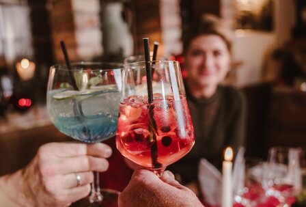 Cocktails in der Hotelbar im Grand Hotel Zwei Hände stoßen mit bunten Cocktails in einer stilvoll gedeckten Hotelbar an.