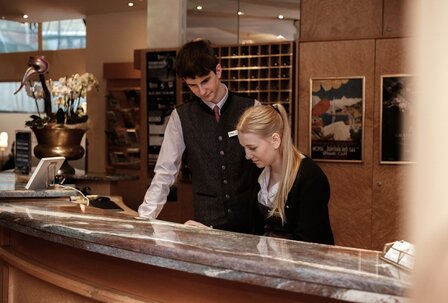 Karriere im Hotel: Rezeption im GRAND HOTEL Zell am See Ein Mitarbeiter und eine Mitarbeiterin arbeiten an der Rezeption des GRAND HOTEL Zell am See.