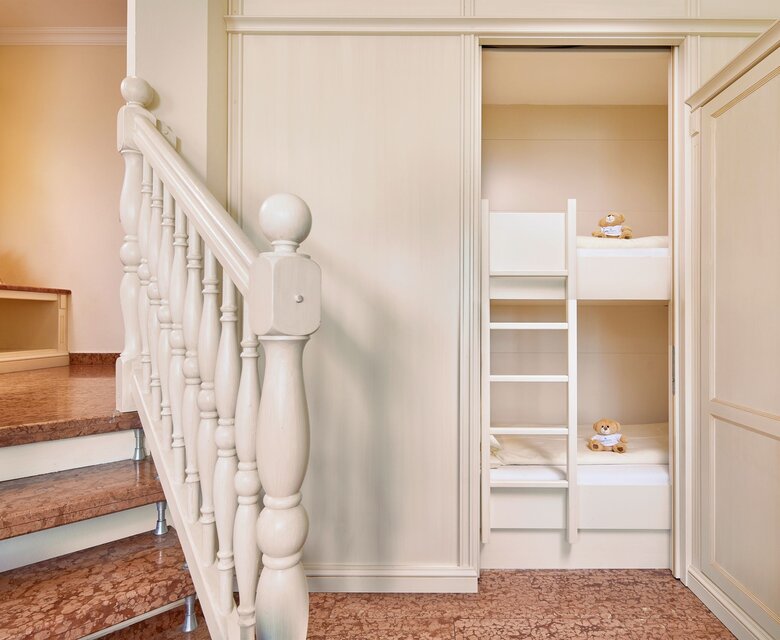 Ein Treppenaufgang führt in ein helles Zimmer mit Etagenbett und weißem Einbauschrank.