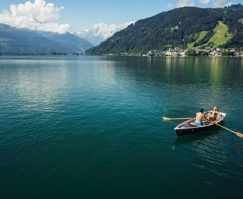 Ein Ruderboot mit zwei Personen liegt auf dem ruhigen Zeller See vor Bergkulisse.