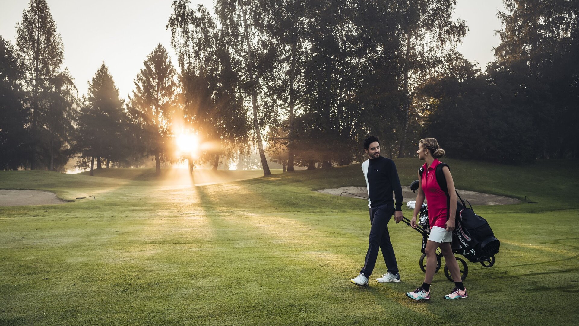 Zwei Golfer gehen mit ihrem Equipment über das Fairway im warmen Abendlicht auf dem Golfplatz.