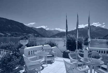 Eine Terrasse mit Tischen und Stühlen blickt auf den Zeller See und die umliegenden Berge.