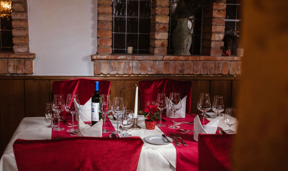 A set table with red chair covers and a wine bottle stands in the wine cellar of GRAND HOTEL Zell am See.