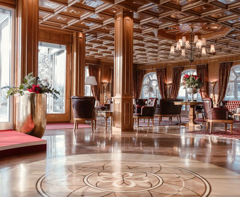 Eine elegante Lounge mit Holzdecke, Sesseln und großen Fenstern im GRAND HOTEL Zell am See.