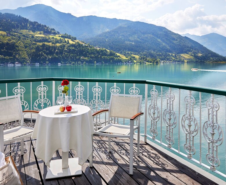 Ein Balkon mit Tisch, zwei Stühlen und Blick auf den Zeller See und die Berge.
