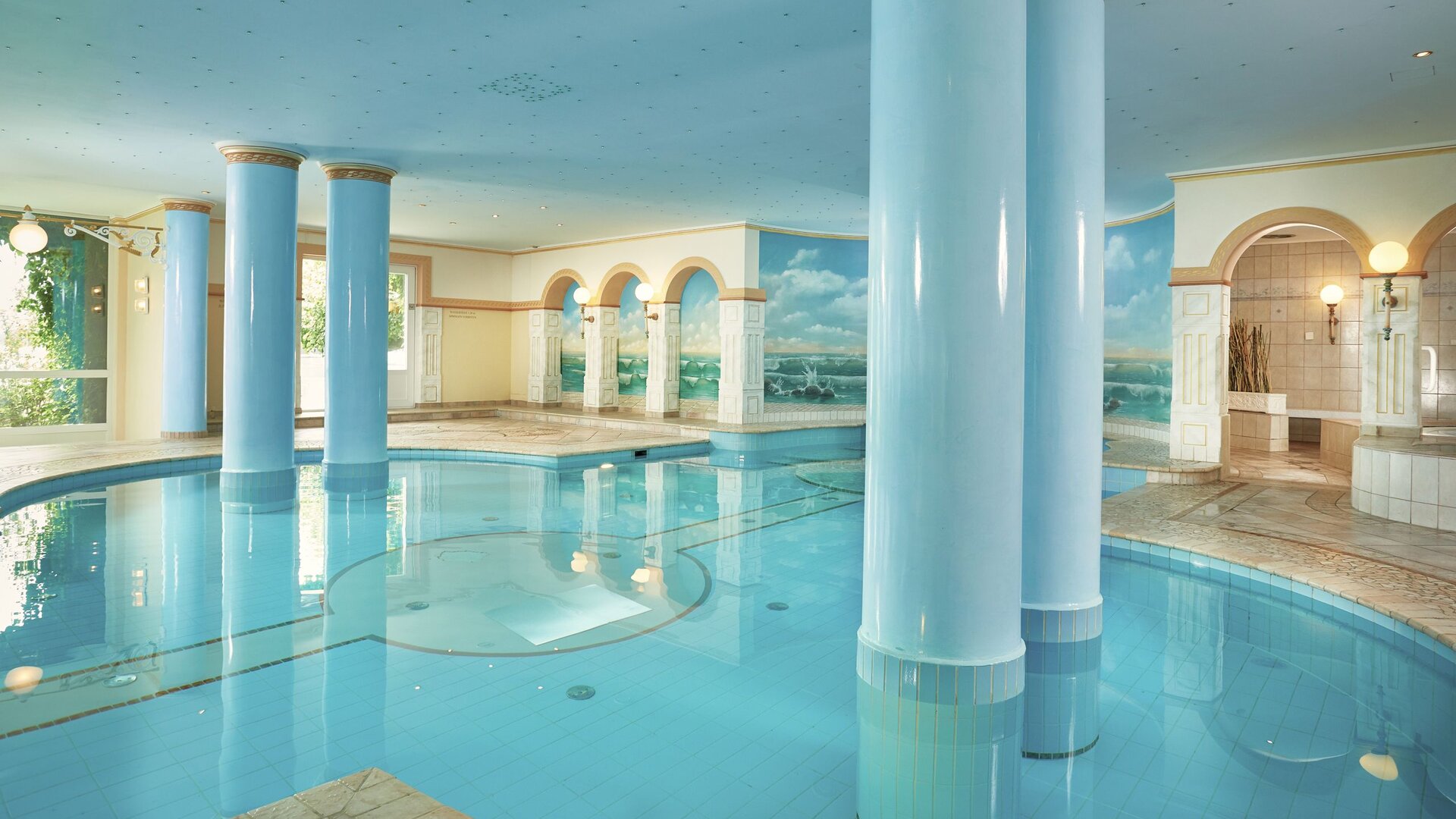 Ein heller Innenpool mit Säulen, Rundbögen und Mosaikboden im Classic Family Spa des GRAND HOTEL Zell am See.