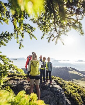 Drei Wandernde stehen auf einem Felsen mit Blick über die Berge und das Tal nahe dem Zeller See.