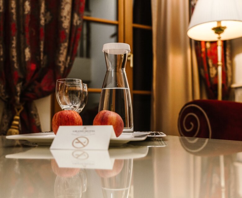 Auf dem Tisch stehen Wasser, ein Glas und Obst in einem Hotelzimmer des GRAND HOTEL Zell am See.