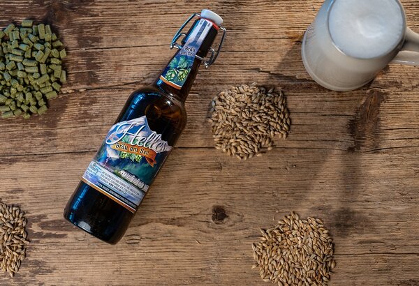 Eine Bierflasche, Malz und Hopfen liegen auf einem rustikalen Holztisch neben einem Schaumglas.