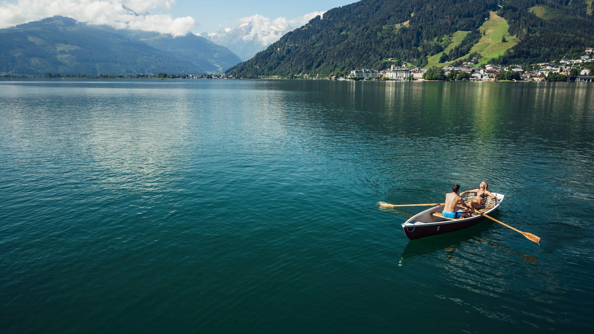 A rowboat with two people on Lake Zell, set against mountains and the lakeside village.