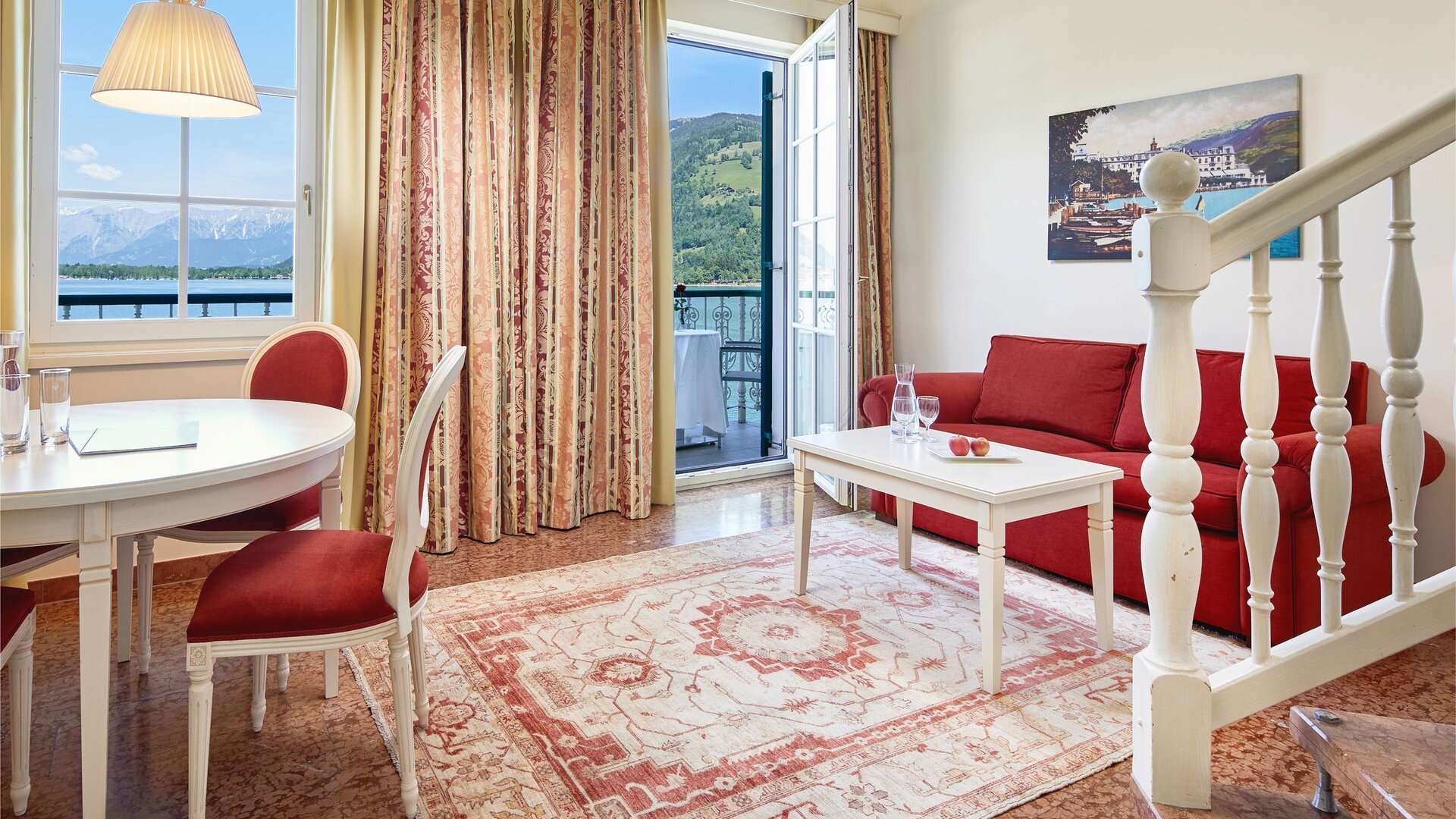 Ein Familienzimmer mit rotem Sofa, rundem Tisch und Blick auf den See durch das Fenster.