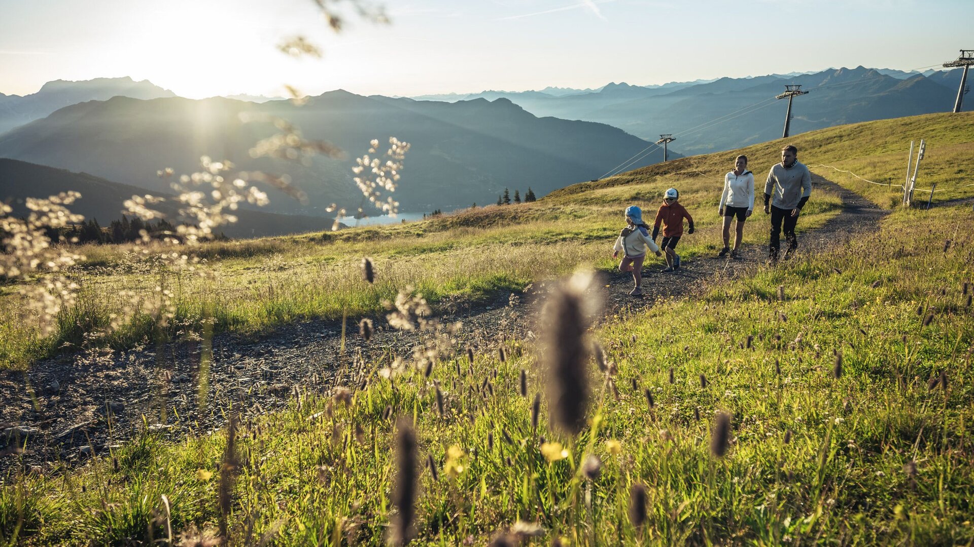 Eine Familie wandert auf einem sonnigen Bergweg mit Blick auf die Alpen und die weite Landschaft rund um Zell am See.